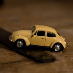 Close-up shot of a yellow toy Volkswagen Beetle on a wooden background, emphasizing detail and design.