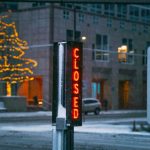 Snowy evening in Minneapolis featuring an illuminated closed sign and decorated trees.