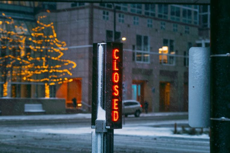Snowy evening in Minneapolis featuring an illuminated closed sign and decorated trees.