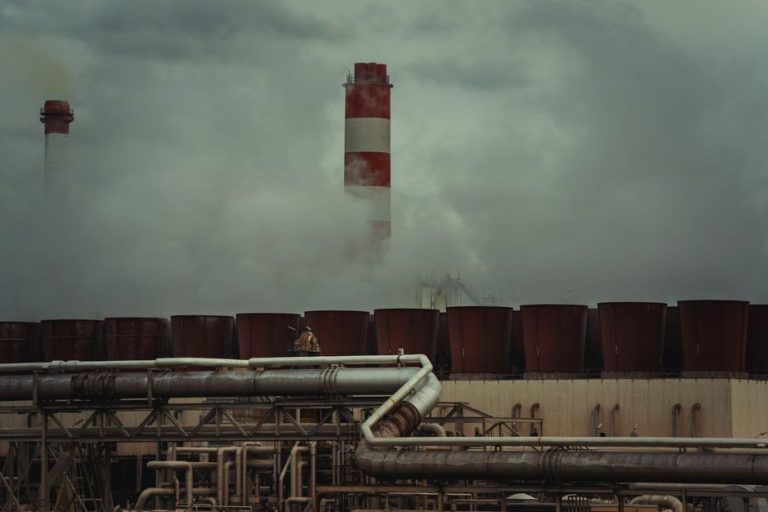 An industrial factory with chimneys releasing smoke under a cloudy sky, conveying urban pollution.
