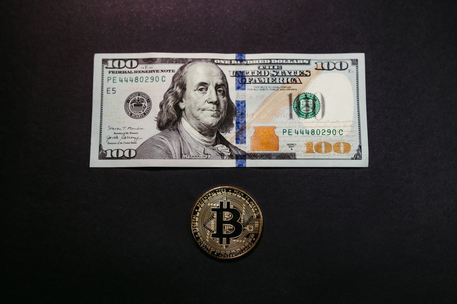 Image of a US 100 dollar bill and a Bitcoin coin on a black background, symbolizing traditional and digital currency.