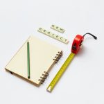 Flat lay of a notebook, pencil, tape measure, and scrabble tiles spelling 'new project'. Ideal for creative work concepts.