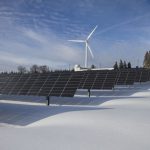 Solar panels and wind turbine in a snowy landscape, showcasing renewable energy sources.