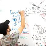 A man engages in brainstorming, writing on a whiteboard filled with creative ideas and sketches.