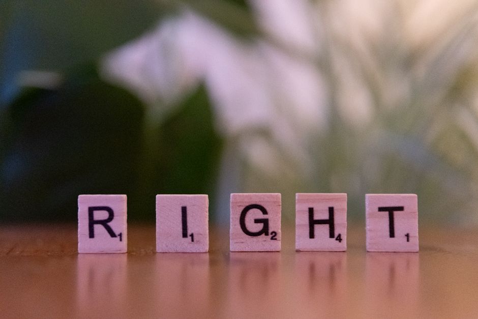 Wooden Scrabble tiles spelling 'Right' on a wooden surface with blurred background.