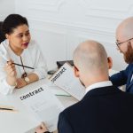 Three business professionals in discussion over a contract in a modern office setting.