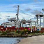Automated container terminal at Port of Melbourne with cranes and containers under a cloudy sky.