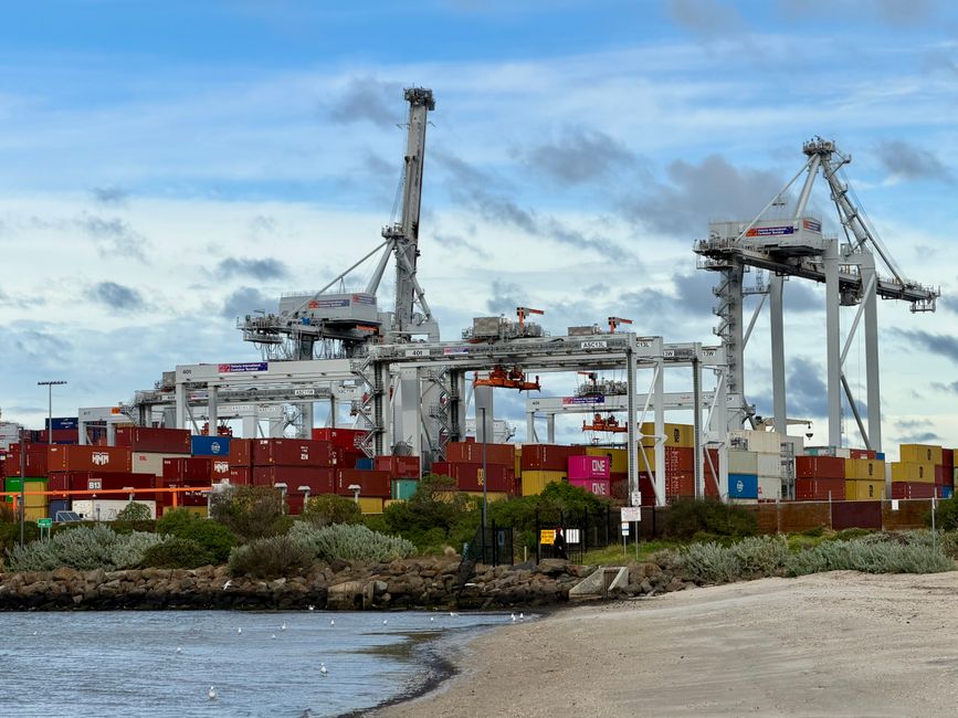 Automated container terminal at Port of Melbourne with cranes and containers under a cloudy sky.