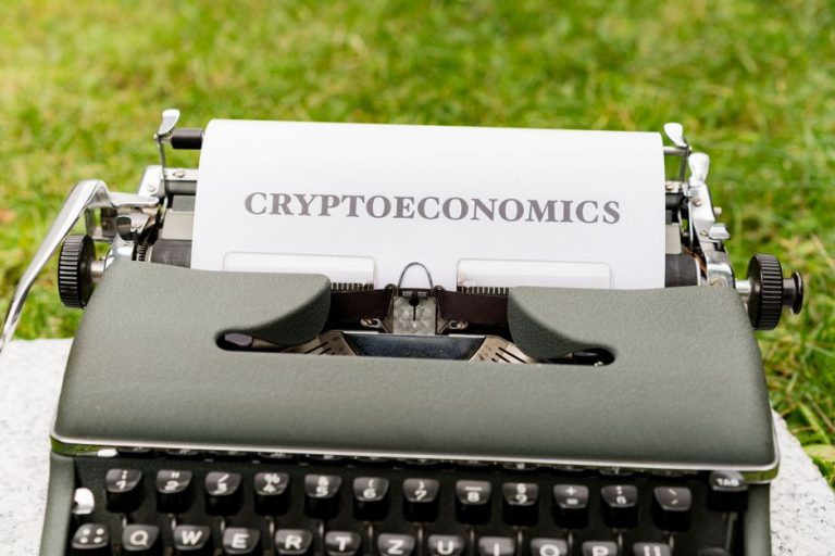 An antique typewriter with cryptoeconomics text on paper against a grassy background.