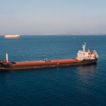 Aerial view of a cargo ship sailing in the open sea under clear skies, showcasing maritime transport.