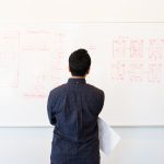 DeFi and Systems Thinking: The Future of Capital Allocation Man analyzing design flowchart on whiteboard in a professional office setting.