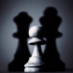 Moody black and white photograph of a chess pawn highlighting strategy and shadow play.