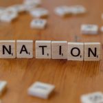 Scrabble tiles spelling 'NATION' on a wooden table, symbolizing patriotism.