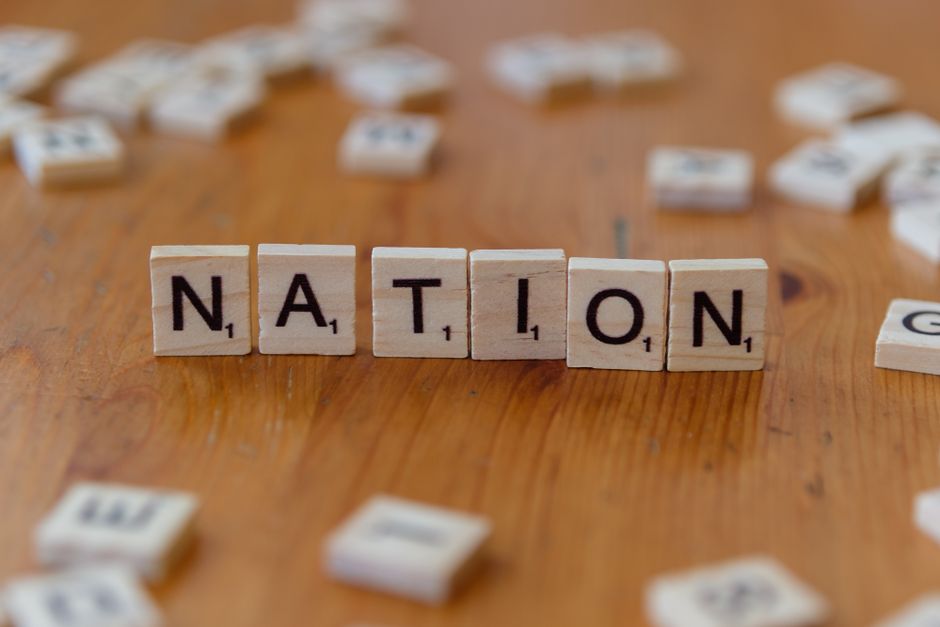 Scrabble tiles spelling 'NATION' on a wooden table, symbolizing patriotism.