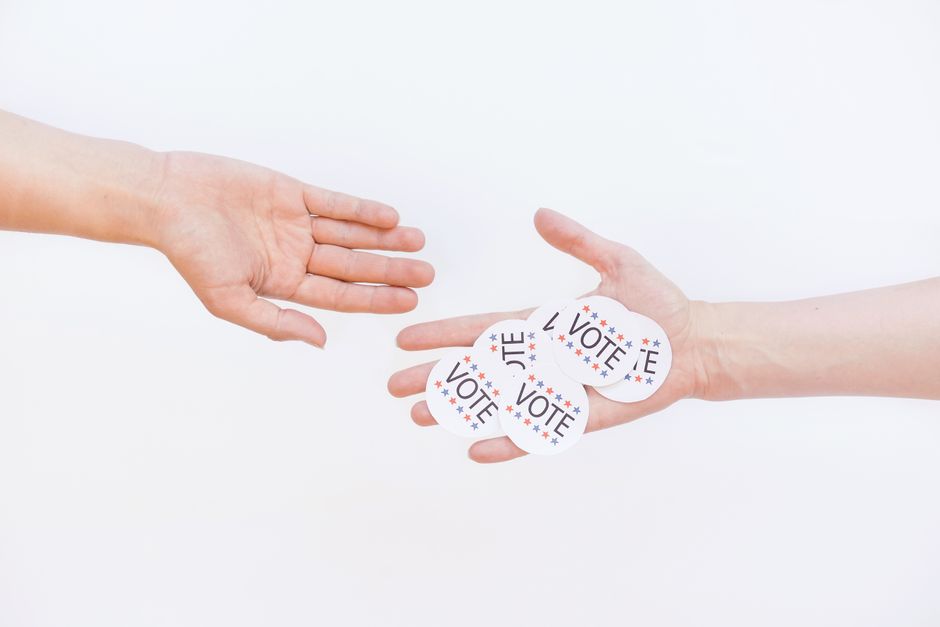 Close-up of hands exchanging vote stickers, symbolizing engagement in democratic election.