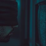 Digital-First Culture: The Hidden Integration Tax Explained A close-up of a blindfolded man facing a static television screen in a dark room.