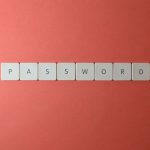 Focus on password security with white keyboard tiles spelling 'PASSWORD' on a coral background.