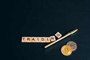 Bitcoin and trading concept shown with coins, pen, and letter tiles on a dark background.