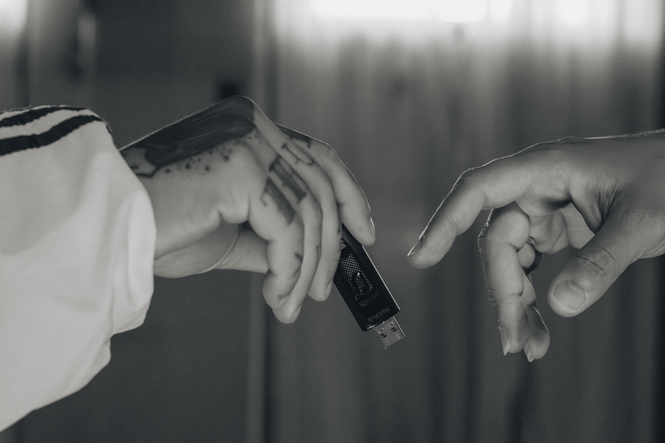 Close up view of two hands exchanging a USB drive against a blurred background.
