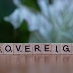 Close-up of wooden Scrabble tiles spelling 'sovereign' on a table with blurred green background.