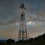 A communication tower silhouetted against a stunning starry night sky with the Milky Way.