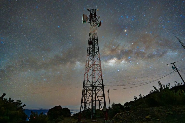 A communication tower silhouetted against a stunning starry night sky with the Milky Way.