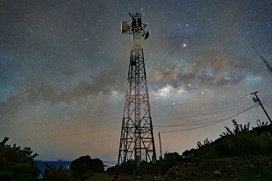 A communication tower silhouetted against a stunning starry night sky with the Milky Way.