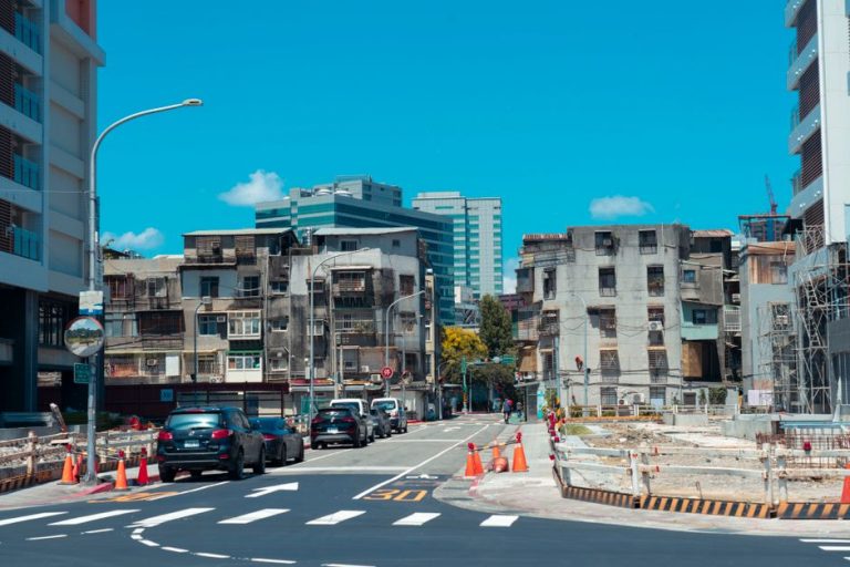 A vibrant urban street with cars, construction, and classic city buildings under a clear blue sky.