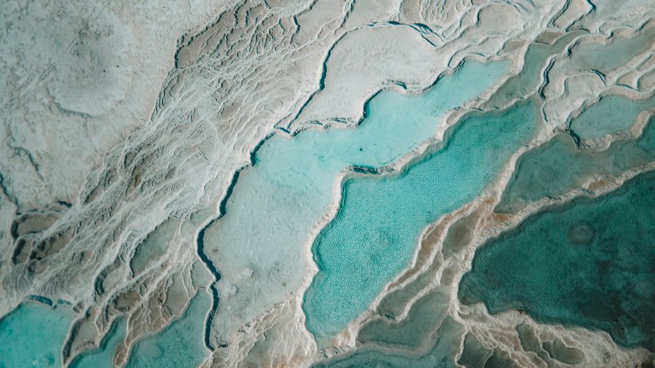 A stunning aerial shot of turquoise thermal pools surrounded by white limestone formations, creating a natural abstract pattern.