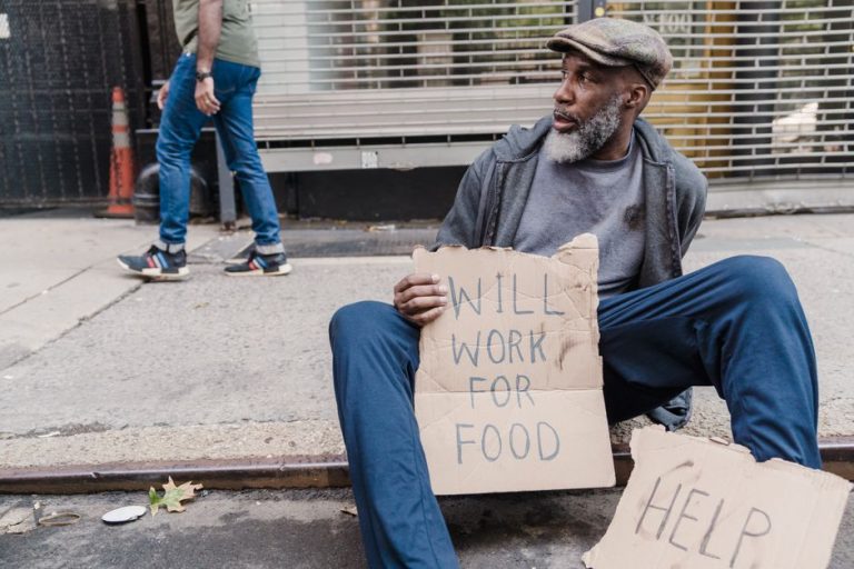 African American man holding a sign seeking help on the sidewalk, representing poverty and homelessness.