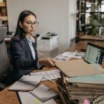 Businesswoman working at a wooden desk with documents and laptop in a modern office.