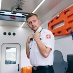 Paramedic standing inside the ambulance van, holding a stethoscope, ready for emergency response.