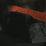 Close-up of glowing hot metal bar on black anvil in a forge setting.