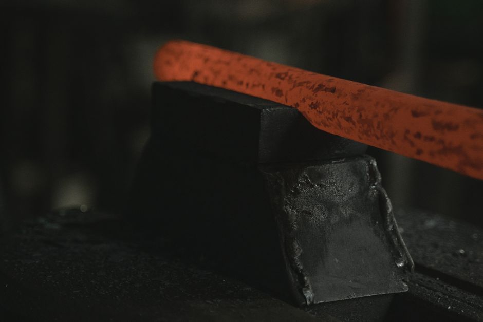 Close-up of glowing hot metal bar on black anvil in a forge setting.