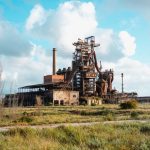 An abandoned factory amid a grassy landscape, showcasing industrial decay.