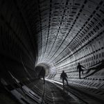 Three silhouetted figures explore a futuristic tunnel with dramatic lighting.