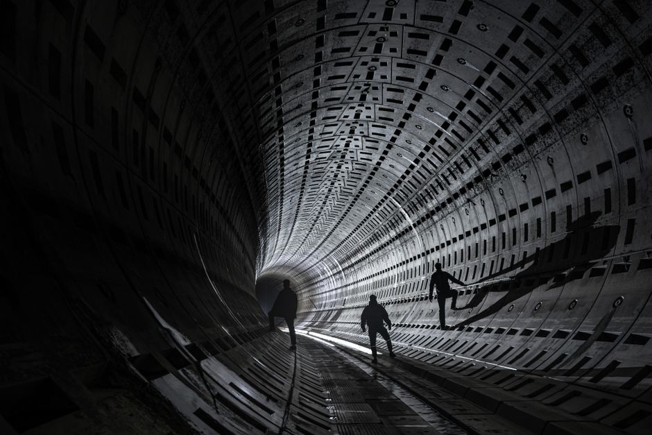 Three silhouetted figures explore a futuristic tunnel with dramatic lighting.