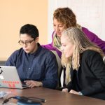 Team of three people collaborating on a laptop in an office setting.