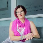 Executive Identity Security: Protecting Your Digital Strategy Portrait of a confident woman sitting indoors wearing glasses and pink scarf.