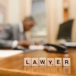 Wooden letter tiles spelling 'LAWYER' on a desk, with blurred office setting in the background.