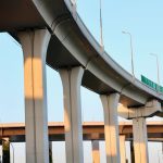 Aerial view of a modern highway overpass with towering concrete pillars at sunset.