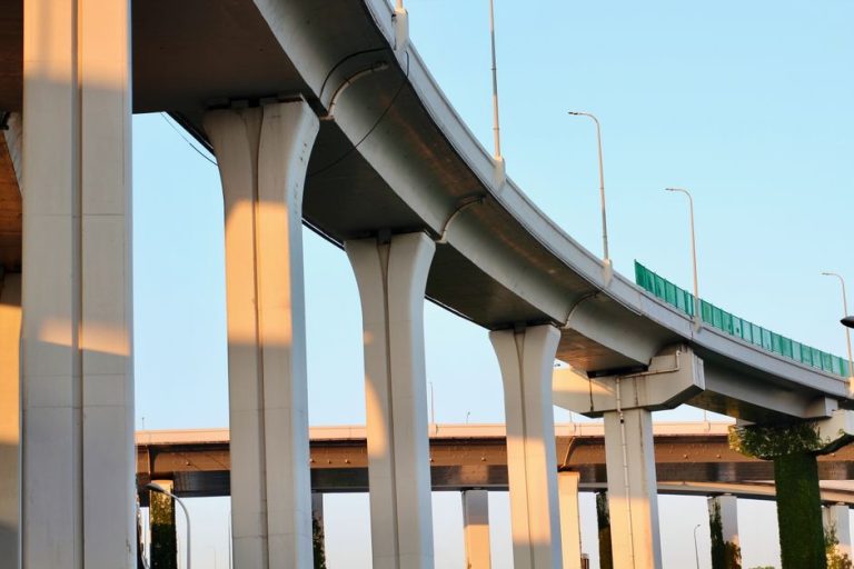 Aerial view of a modern highway overpass with towering concrete pillars at sunset.