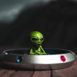 Extraterrestrial Resource Law: A Guide for Strategic Leaders Green alien toy sitting in a spaceship-themed ashtray, outdoors with dramatic lighting.