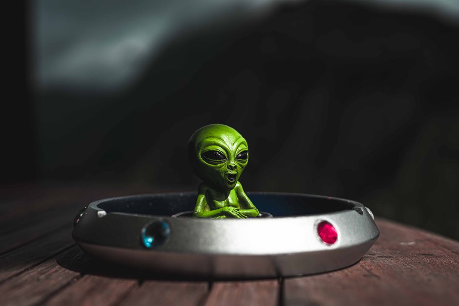 Green alien toy sitting in a spaceship-themed ashtray, outdoors with dramatic lighting.