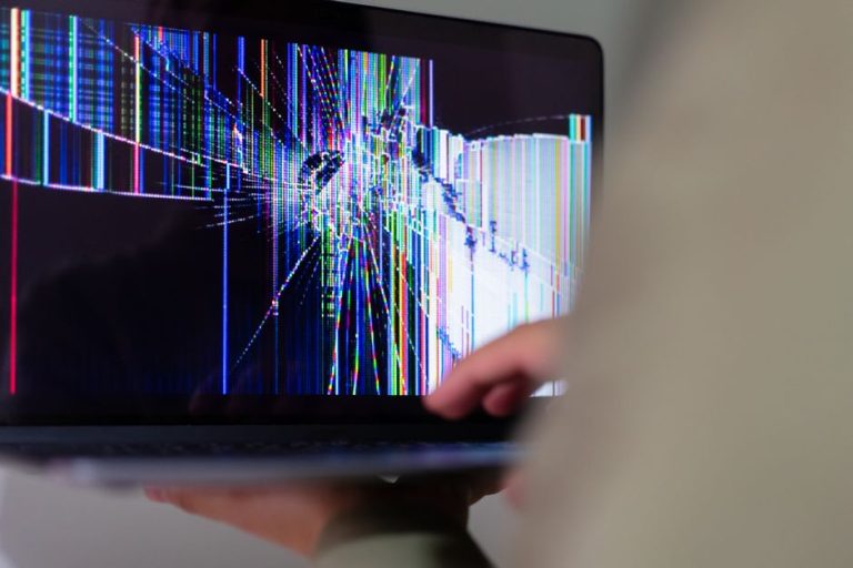 A close-up view of a cracked laptop screen displaying colorful digital distortion.