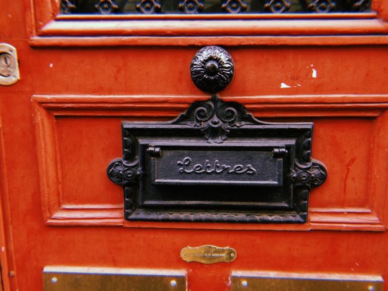 Classic French letterbox on a red wooden door in Paris.