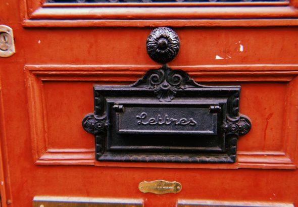 Classic French letterbox on a red wooden door in Paris.
