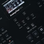 Detailed view of an Analog Four MKII synthesizer control panel, featuring buttons and screen.