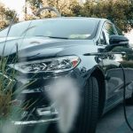 Fusion Energy: Strategic Shifts for the Future of Industry A black hybrid car charging at an outdoor station surrounded by greenery.