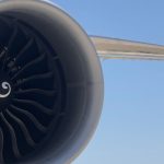 Detailed view of an aircraft jet engine with turbine blades against a clear blue sky.
